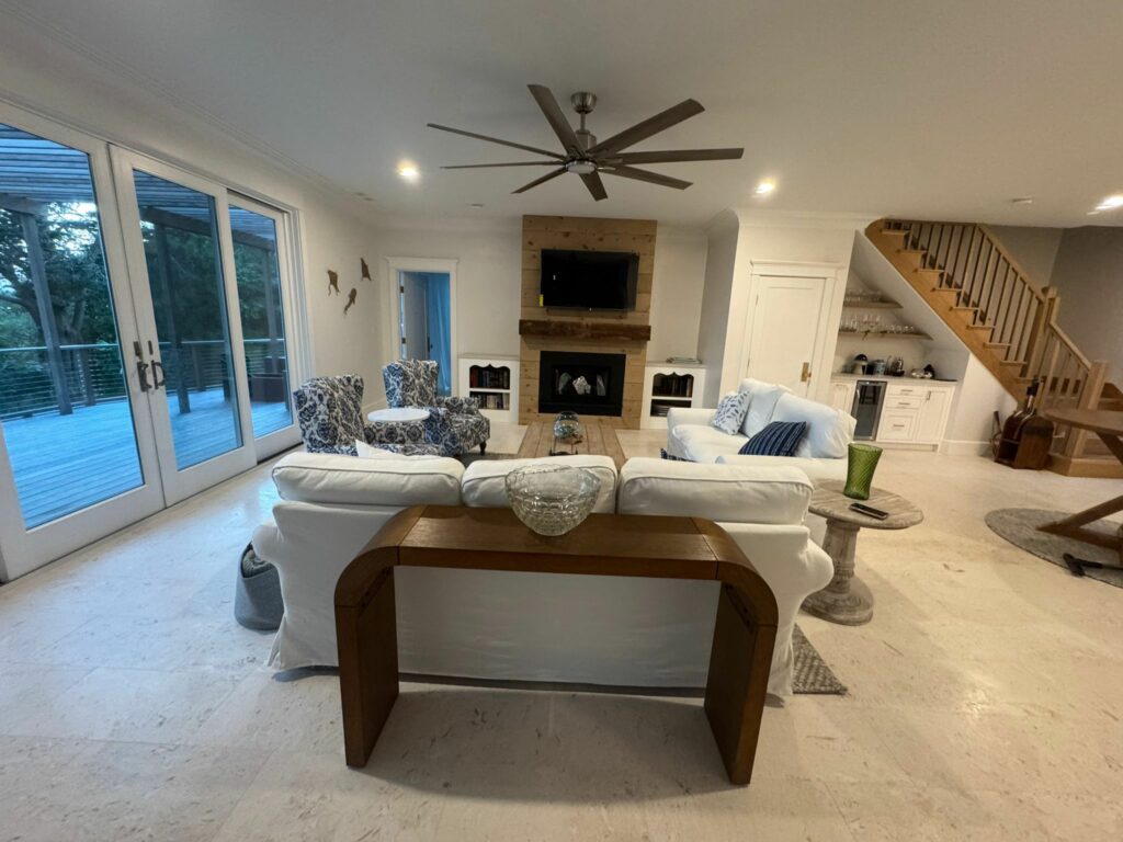 Modern living room with white sofas, a fireplace, TV, large windows, and a staircase on the right—kept inviting with regular cleaning for a fresh and tidy space.