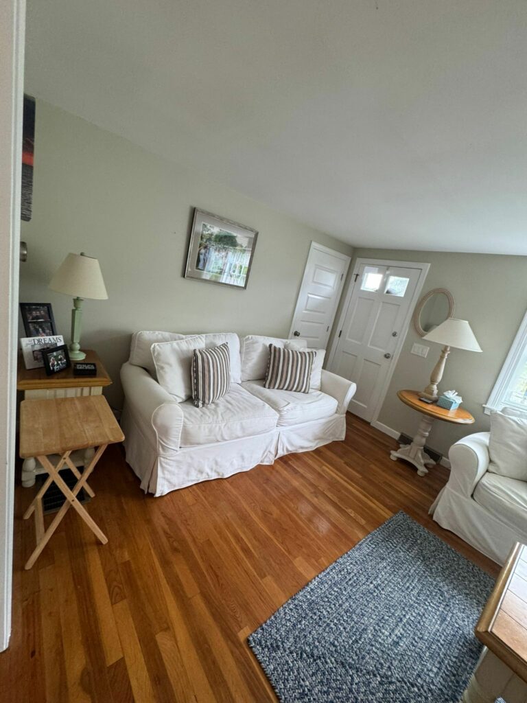Cozy living room with white couches, striped pillows, wooden tables, and a blue rug on hardwood floor—kept spotless with regular house cleaning for a fresh, inviting space.